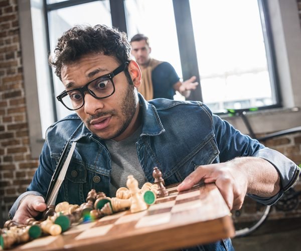 scared man holding chess board with friend behind